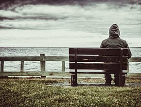 Man sitting alone on bench overlooking a gray sky and sea